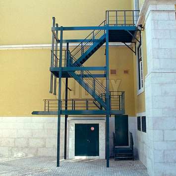 Anti-inbraak trappen met ophaalbare traparm Zwart anti-inbraak evacuatietrap met ophaalbare traparm geïnstalleerd in een voetgangersstraat aan de achterkant van een gebouw.